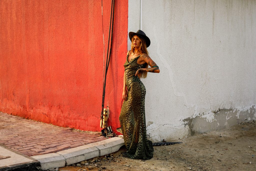 Fashionable woman in a stylish dress stands confidently against a textured wall.